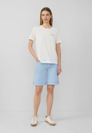 T-shirt en coton blanc avec un petit graphique sur la poitrine, associé à un short bleu clair avec des revers. Des baskets blanches complètent le look.