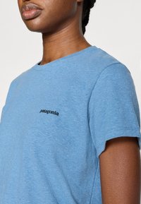 Ανοιχτό γαλάζιο μπλουζάκι από μαλακό ύφασμα. Διαθέτει στρογγυλή λαιμόκοψη και κοντά μανίκια. Μαύρο λογότυπο Patagonia στην αριστερή πλευρά του στήθους.