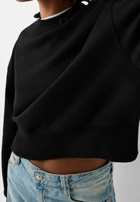 Sudadera corta negra con un tejido texturizado, cuello redondo y dobladillo acanalado, combinada con unos jeans de mezclilla azul claro.