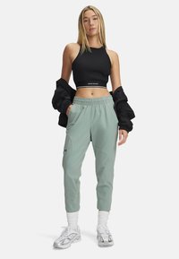 Black ribbed crop top, light green tapered joggers with side pockets, elastic waistband, and logo. White socks and silver athletic shoes.