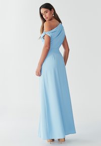 Helehall sinine, õlgadeta kleit, millel on voltidega kangas ja voolav siluett. Sile tekstuur, pikk lõige, kombineeritud beežide kontsadega.