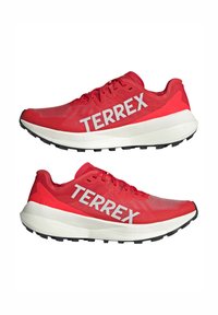 Scarpe sportive rosse con tomaia in rete, con il marchio "TERREX" in bianco. Suola intermedia spessa e bianca con suola esterna nera testurizzata per una migliore aderenza.