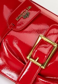 Rode lakleren handtas met een klep sluiting, gouden hardware en een vierkante gesp. Bevat een geperst logo en een gladde, glanzende textuur.