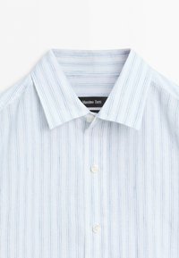 White dress shirt with thin vertical blue stripes, pointed collar, and white buttons, labeled Massimo Dutti inside the collar.
