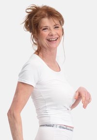 Witte t-shirt met korte mouwen en een ronde hals, gedragen met witte ondergoed met een blauw en zwart merklabel. Soepele textuur.