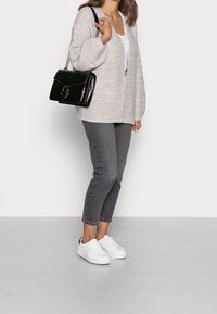 Jasnoszary sweter z dzianiny nałożony na biały top, w zestawieniu z szarymi krótkimi dżinsami i białymi trampkami. Czarnej, fakturowanej torebki dopełnia całość.