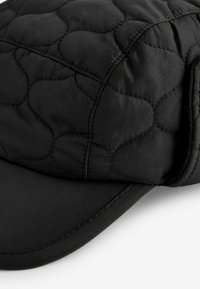 Casquette noire matelassée avec une surface texturée, présentant une visière courbée et des détails de couture simples. Le tissu doux crée un aspect rembourré.