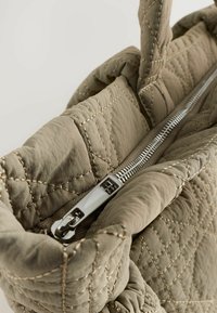 Gros plan sur un sac à main en olive matelassé avec une fermeture éclair en argent, mettant en valeur son tissu texturé et son ouverture en haut, révélant l'intérieur.
