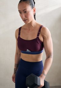 Reggiseno sportivo in bordeaux e blu con spalline regolabili; texture liscia; abbinato a leggings blu navy; include un manubrio in una mano.