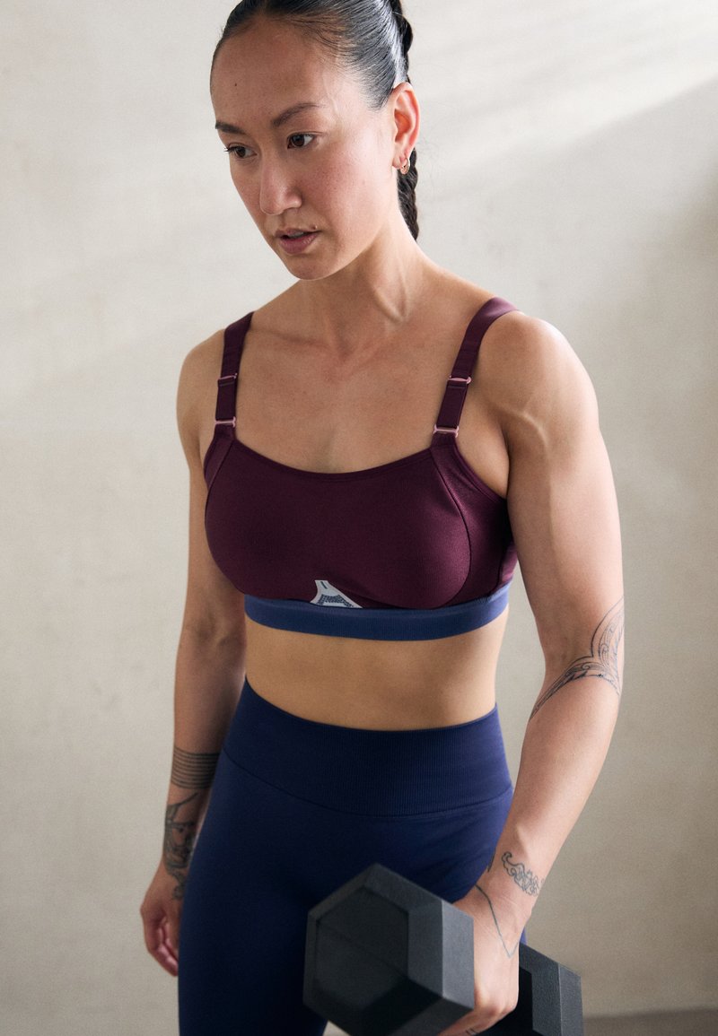 Reggiseno sportivo in bordeaux e blu con spalline regolabili; texture liscia; abbinato a leggings blu navy; include un manubrio in una mano.
