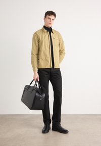 Veste légère beige avec une fermeture éclair, col roulé noir, pantalon noir et sac en cuir noir. Texture lisse et design minimal.