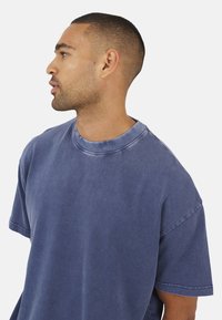 T-shirt oversize di colore blu sbiadito, con collo rotondo e maniche corte, realizzata in un tessuto morbido e testurizzato.