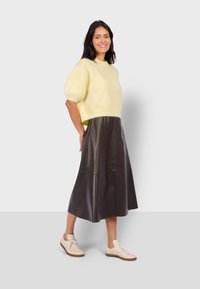 Suéter amarillo corto de punto con mangas abullonadas, combinado con una falda de cuero oscura y zapatillas beige, resaltando un ajuste relajado y una textura suave.