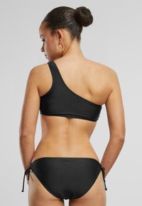 Black one-shoulder bikini top with smooth fabric and a matching tied bikini bottom. Features minimalistic design and seamless edges.