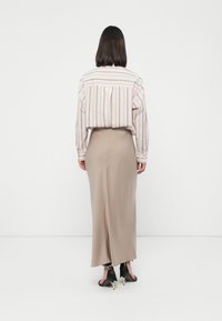 Gestreifte Bluse in Pastellfarben, kombiniert mit einem beigen, knöchellangen Rock. Schwarze High-Heels runden das Outfit ab.