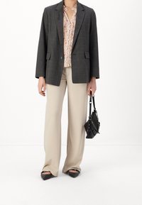 Blazer grigio a quadri, blouse floreale, pantaloni beige a gamba larga, scarpette nere a punta e una piccola borsa nera con dettaglio a catena.