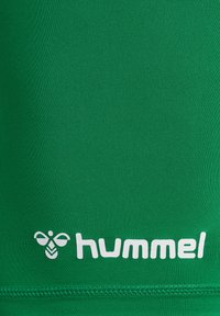 T-shirt de sport vert en tissu lisse et extensible. Présente un logo "hummel" blanc et une icône d'abeille près de l'ourlet inférieur.