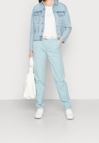 Pantalon en coton bleu clair associé à une veste en jean claire, un t-shirt blanc et un sac en toile crème. Des baskets blanches complètent la tenue.