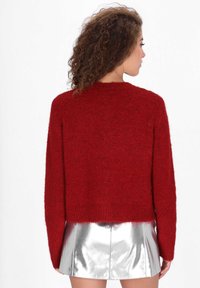 Czerwony, puszysty sweter z długim rękawem i skróconym hemem, w połączeniu z błyszcząca, srebrna metaliczna mini spódnicą. Tekstura miękka i przyjemna w dotyku.