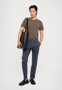 Brun kortärmad t-shirt, marinblå byxor, svart läderväska och svarta skor. Slät tygkvalitet och skräddarsydd passform med minimala detaljer.