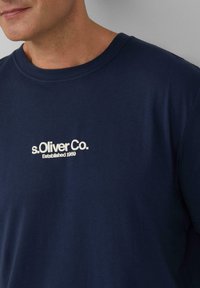 Marineblauwe T-shirt van zacht stof met een ronde halslijn en een witte bedrukte logo "s.Oliver Co. Opgericht 1969" op de voorkant.