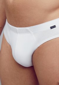 White cotton brief with elastic waistband featuring a small logo tag. Smooth texture and fitted design highlighting a seamless fit.