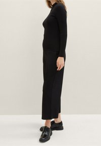 Maglione nero a coste con maniche lunghe abbinato a pantaloni neri a gamba larga e scarpe nere lucide. Design semplice, texture liscia e colore uniforme.