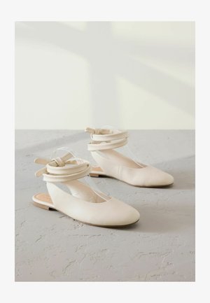 Beige Ballerinas mit einer runden Zehenpartie, aus weichem Leder gefertigt und mit einem transparenten Riemen-Design. Schlitzseitenteile mit geknoteten Akzentdetails. Flache Sohle.
