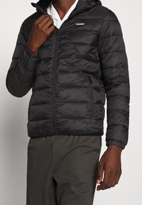 Czarna kurtka puchowa z zamkiem z przodu, poziomym pikowaniem, kapturem i bocznymi kieszeniami; gładka faktura i lekki materiał.