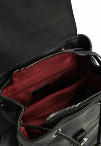 Interno di una borsa in pelle nera con una texture liscia, caratterizzato da un rivestimento in tessuto rosso e numerose tasche con zip per l'organizzazione.