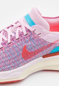 Běžecká obuv Nike s pleteným svrškem v růžové a modré barvě, s texturovaným vzorem, růžovými tkaničkami a viditelným oranžovým logem Swoosh.
