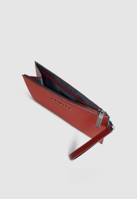 Bolso de mano de cuero rojo con cierre de cremallera, con un interior azul. El diseño incluye una correa para la muñeca y herrajes metálicos con la marca.