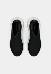 Slip-ons pretos de malha com superfície texturizada, sola de borracha branca e um detalhe preto no calcanhar com texto do logótipo.