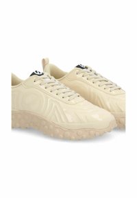 Scarpe da ginnastica beige con finitura lucida, design texturizzato e suole in gomma tonde. Presentano lacci e un logo nero sulla linguetta.