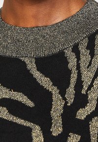 Maglione nero con un motivo testurizzato dorato che ricorda linee astratte. Il collo a coste dorato esalta il design. Materiale in maglia di peso medio.