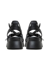 Sandales à plateforme en cuir noir avec découpes ouvertes, brides réglables et un talon texturé. Vue arrière mettant l'accent sur le design et le matériau du talon.