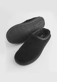 Schwarze Wildlederhausschuhe haben ein plüschiges Innenfutter und eine Gummisohle mit einem gewellten Profil für besseren Halt. Rutschfestes Design mit abgerundeter Zehenpartie.