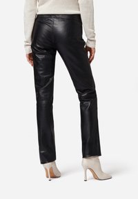 Zwarte leren broek met een aansluitend ontwerp, een gladde textuur en rechte pijpen, gecombineerd met beige hoge hakken.