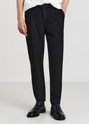 Pantaloni neri su misura con pieghe, realizzati in tessuto liscio. Presentano una vestibilità slim e una fibbia lucida. Abbinati a scarpe di pelle nere.