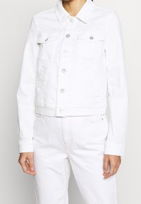 Chaqueta de mezclilla blanca con cuello, cierre frontal de botones, dos bolsillos en el pecho y mangas largas con puños de botón.