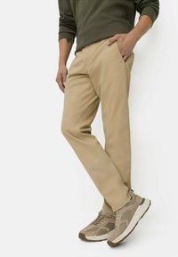 Beige lightweight trousers with front pockets, a straight fit, and subtle stitching details, paired with beige and brown athletic shoes.