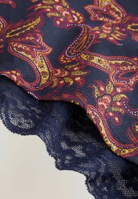 Daugiabriaunio paisley rašto audinys su turtingais raudonais ir auksiniais atspalviais ant tamsiai mėlyno pagrindo, su dekoratyviais nėriniais kraštu.