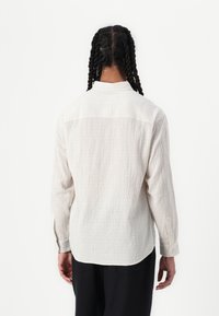 Chemise à manches longues, de couleur claire, avec un motif en grille, un tissu texturé et un empiècement au dos. Elle est dotée de poignets boutonnés et d'une ourlet arrondi.