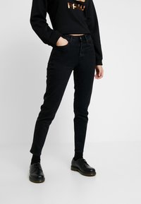 Svarta denimjeans med slim fit, fem fickor och knäppning med knapp, kombinerat med en svart sweatshirt och svarta skor.