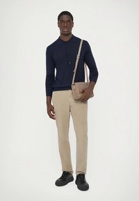 Polo a maniche lunghe blu navy, pantaloni beige aderenti, sneakers nere e una piccola borsa a tracolla marrone chiaro con una tasca frontale.