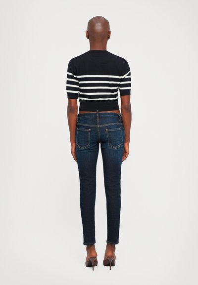 Person standing with back to camera wearing a black and white striped short-sleeve shirt, dark blue jeans, and brown high-heeled shoes.