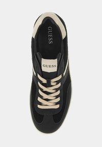 Schwarzer Sneaker aus Wildleder und Leder mit beigen Schnürsenkeln und "GUESS"-Logo auf der Zunge. Verfügt über eine weiße Gummisohle und eine schlanke, abgerundete Form.