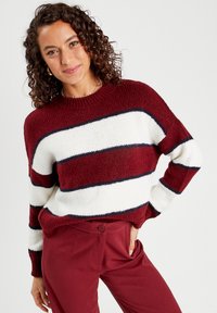 Pull rayé rouge et blanc avec un col rond, coupe ample et poignets côtelés. Associé à un pantalon maroon, mettant en valeur un tricot texturé.