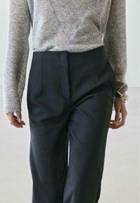 Maglione grigio lavorato a maglia con maniche lunghe abbinato a pantaloni neri lisci a vita alta, con pieghe frontali e tasche laterali.