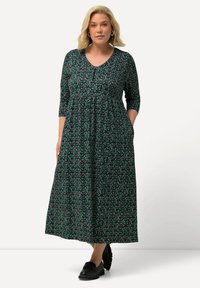 Vestido maxi negro con estampado floral, mangas tres cuartos, escote en V y bolsillos. Material suave, silueta fluida y botones decorativos.
